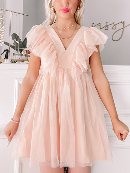 Blush pink tulle dress with ruffled sleeves, shown on a model against a white wall.
