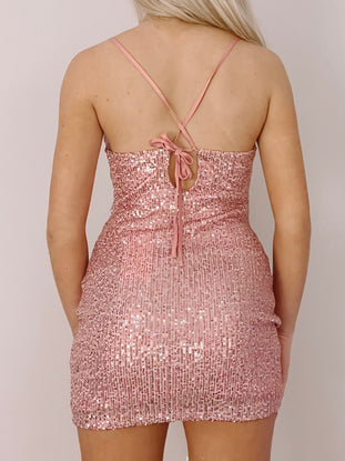 Sparkly rose-gold mini dress with a tie back detail, shown from behind.
