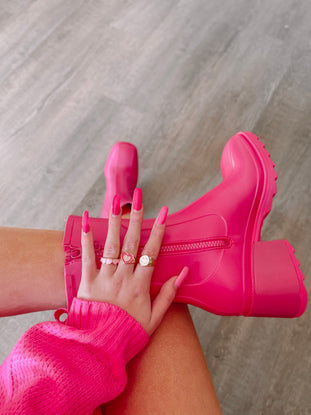 Hot pink rain boots with chunky heels, shown on a model's legs against a neutral background.
