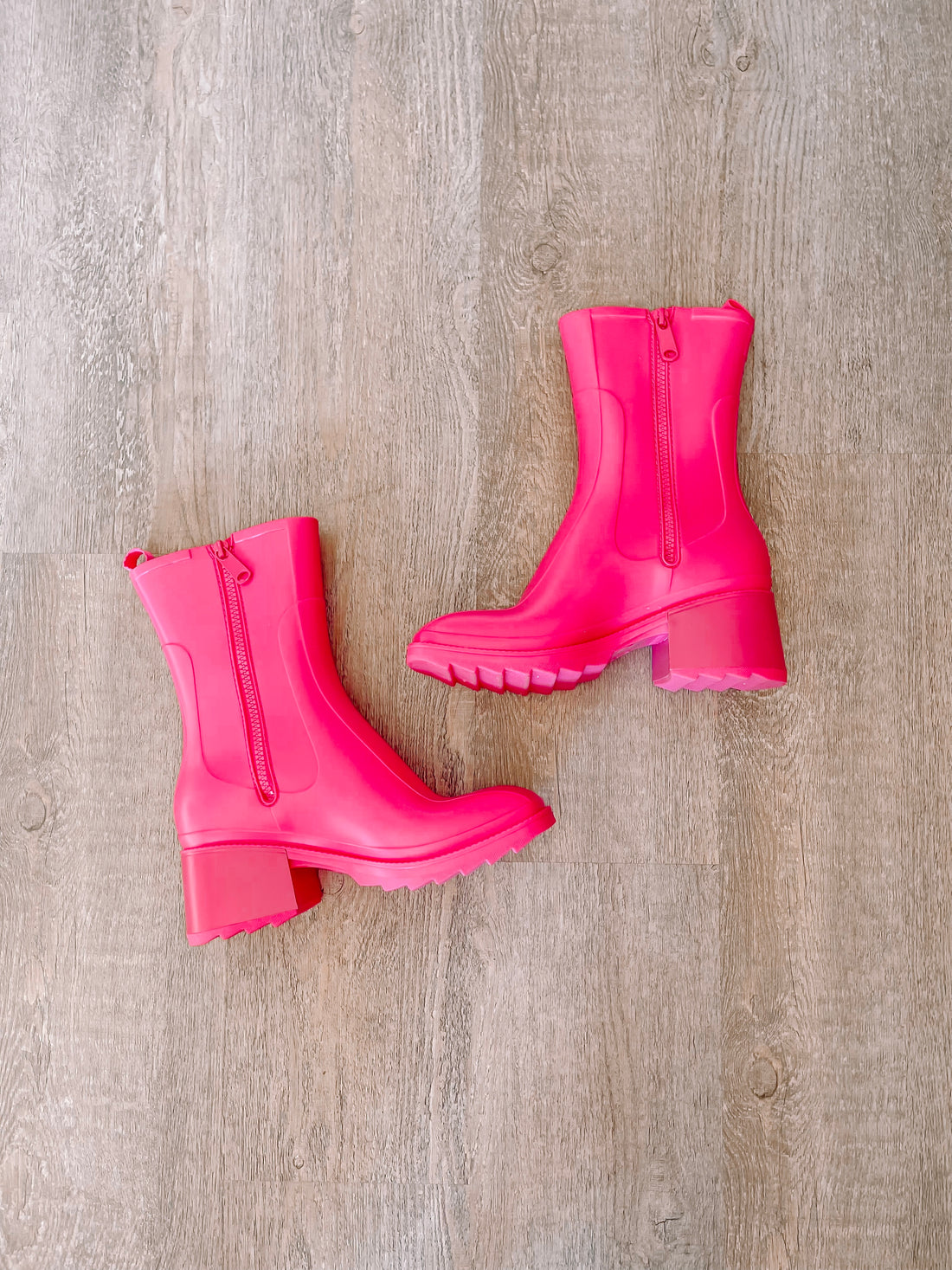 Hot pink rain boots with side zippers, shown on a wood background.
