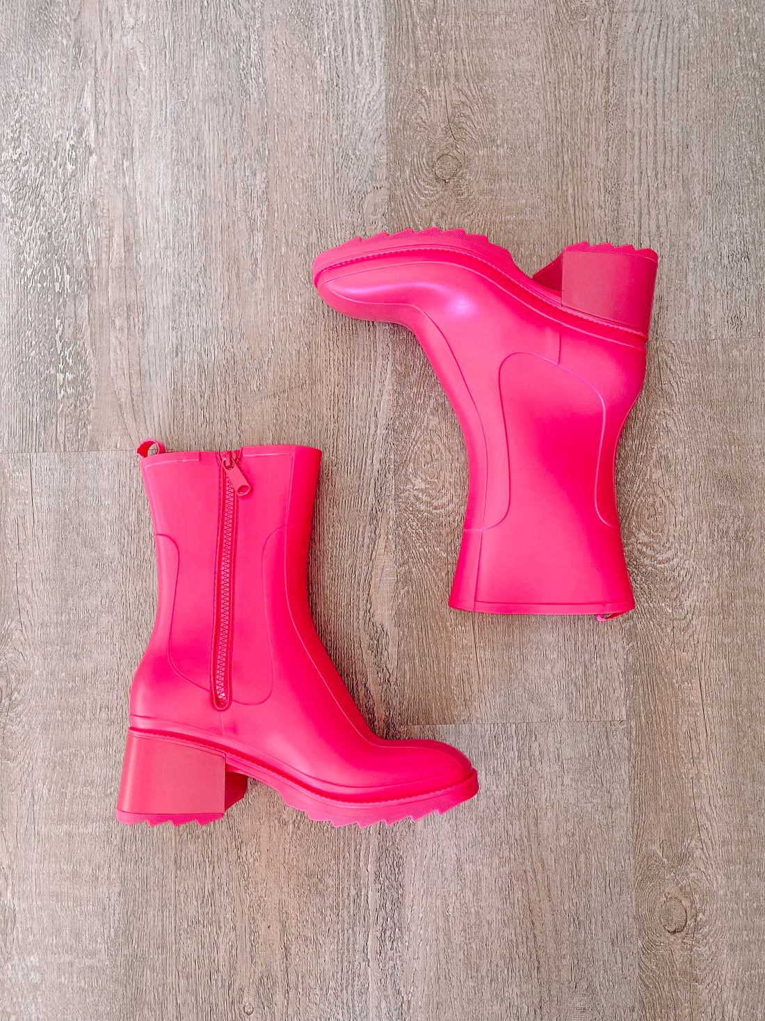 Hot pink rain boots with block heels, shown on wood.
