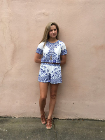 Blue and white patterned crop top and shorts set against a pink wall.
