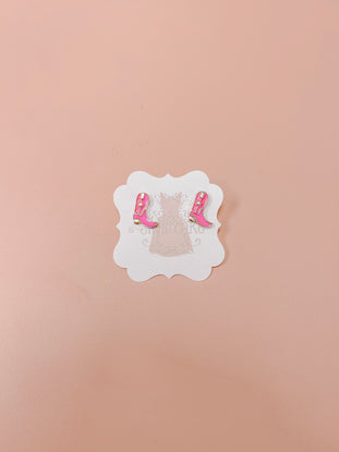 Pink cowboy boot stud earrings displayed on a light pink background.
