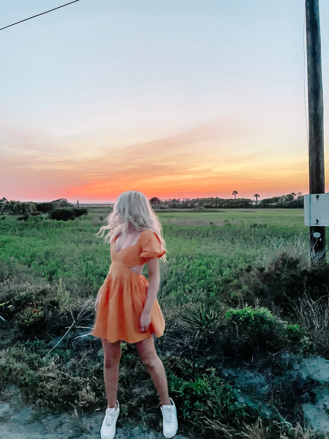 Orange sundress worn outdoors at sunset,  blonde model facing away from camera.
