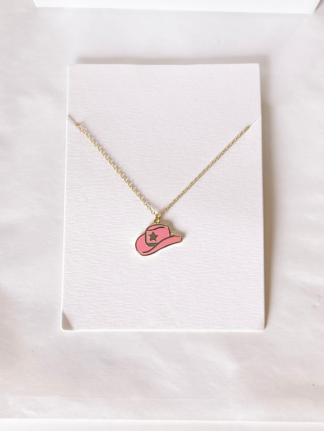 Gold chain necklace with a pink cowboy hat charm.

