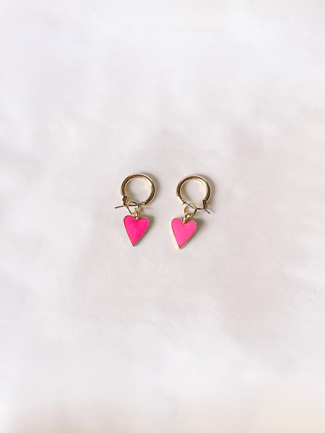 Gold hoop earrings with pink heart charms, shown on a white background.
