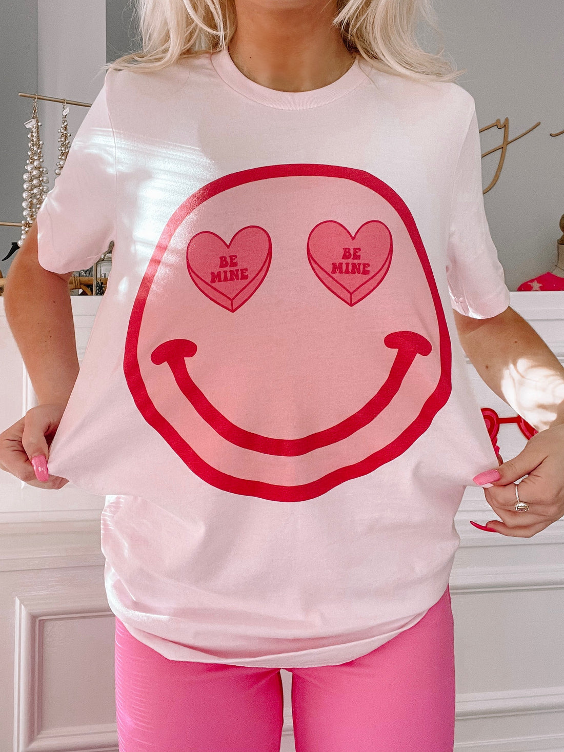 Pink t-shirt featuring a smiley face graphic with candy heart eyes; Valentine's Day themed.
