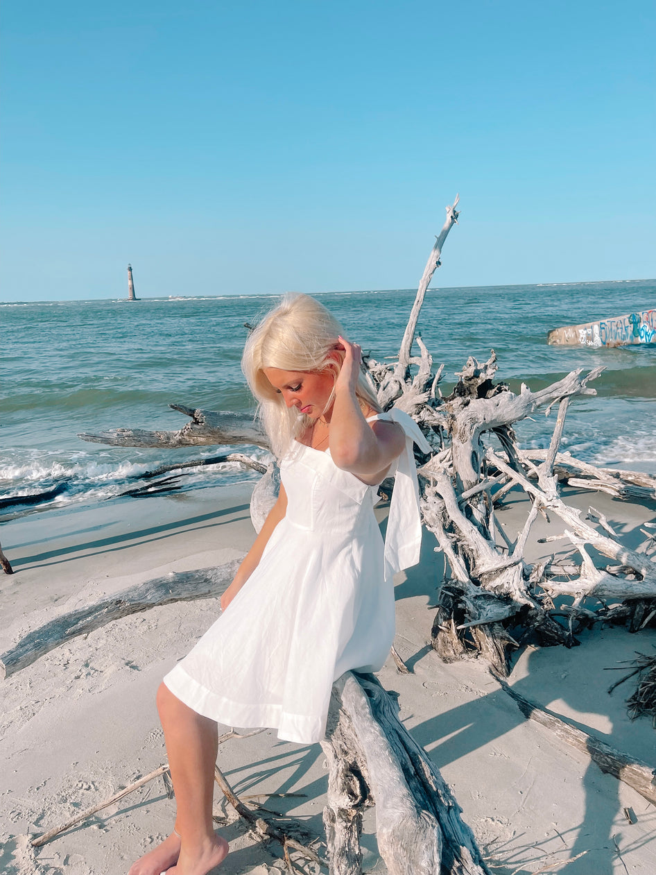 White sundress on beach, driftwood background

