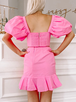 Hot pink puff-sleeve crop top and mini skirt set, shown from the back against a white wall.
