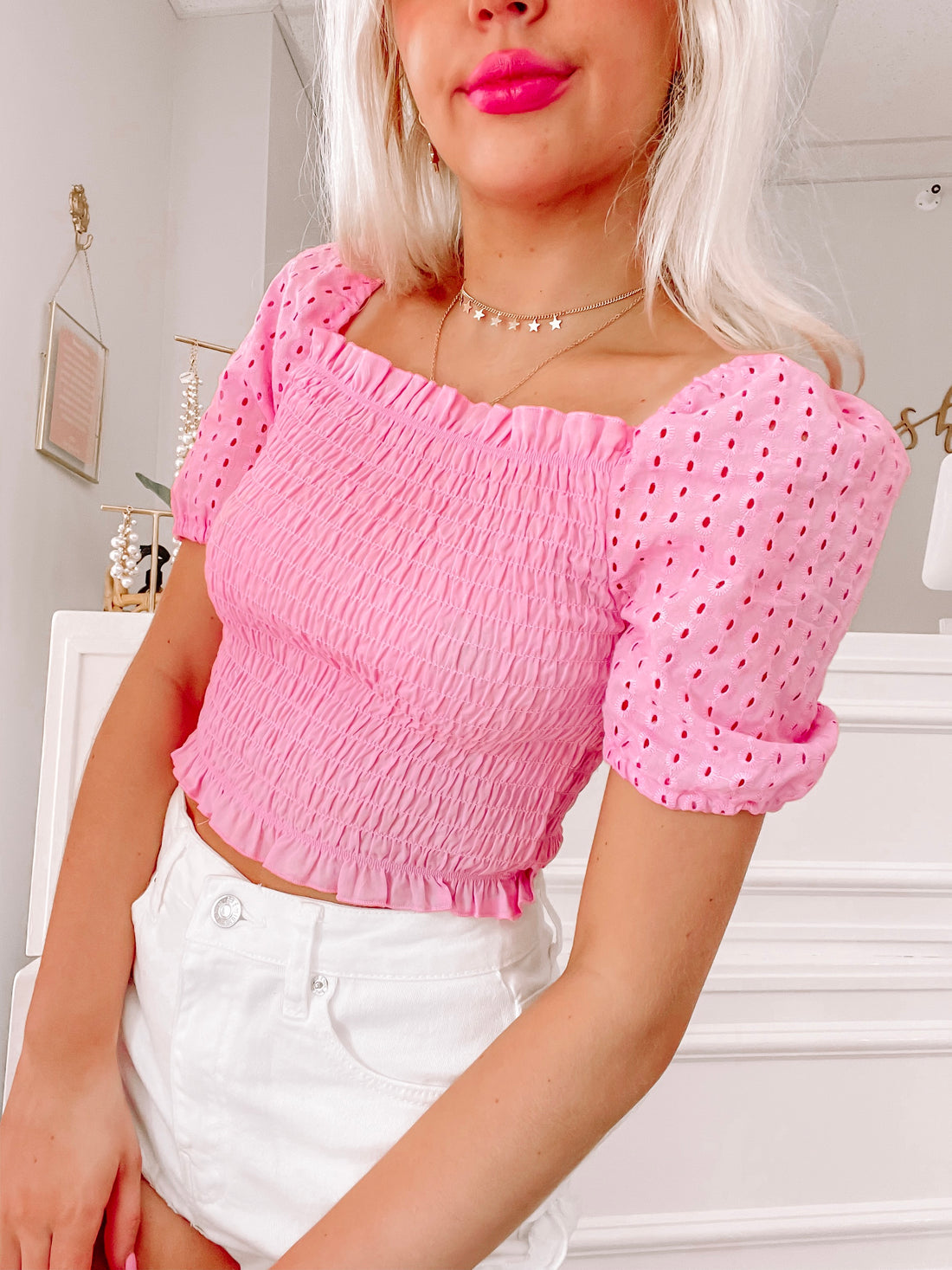 Pink eyelet peasant top with smocked bodice, shown styled with white denim shorts.

