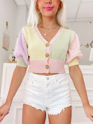 White denim shorts with frayed edges, modeled with pastel cardigan.
