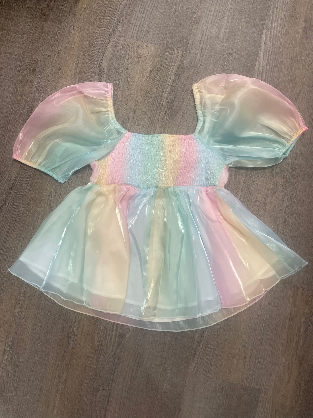 Pastel rainbow ombre blouse with puff sleeves, shown on wood background.
