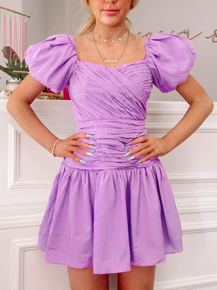 Lilac mini dress with puff sleeves and a fitted bodice, shown on a model against a white background.

