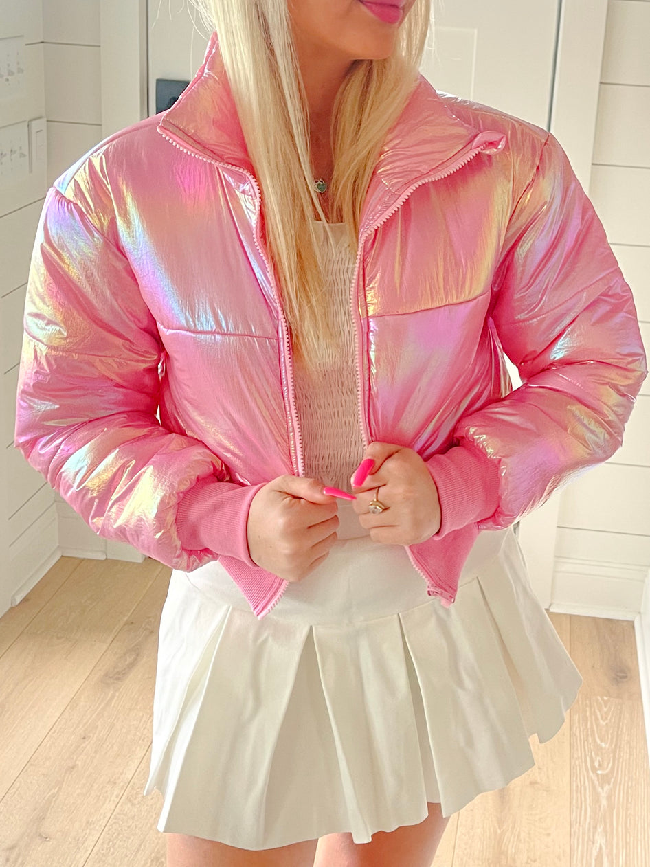 Iridescent pink puffer jacket, cropped length, modeled with white pleated skirt.
