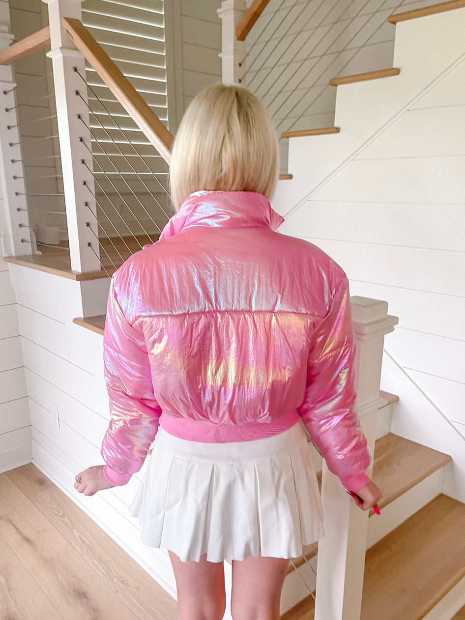 Iridescent pink puffer jacket shown from the back, near a staircase.
