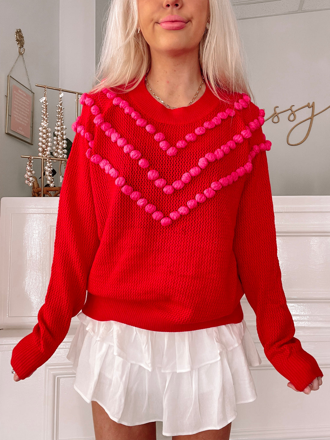 Red Deck the Poms sweater with pink pom-pom detail
