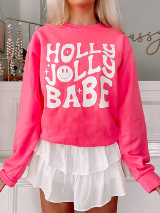 Hot pink sweatshirt with a playful "Holly Jolly Babe" design, featuring a smiley face.
