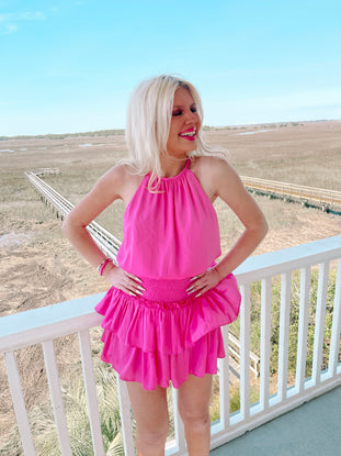 Hot pink tiered mini dress worn outdoors on a deck overlooking marshland.
