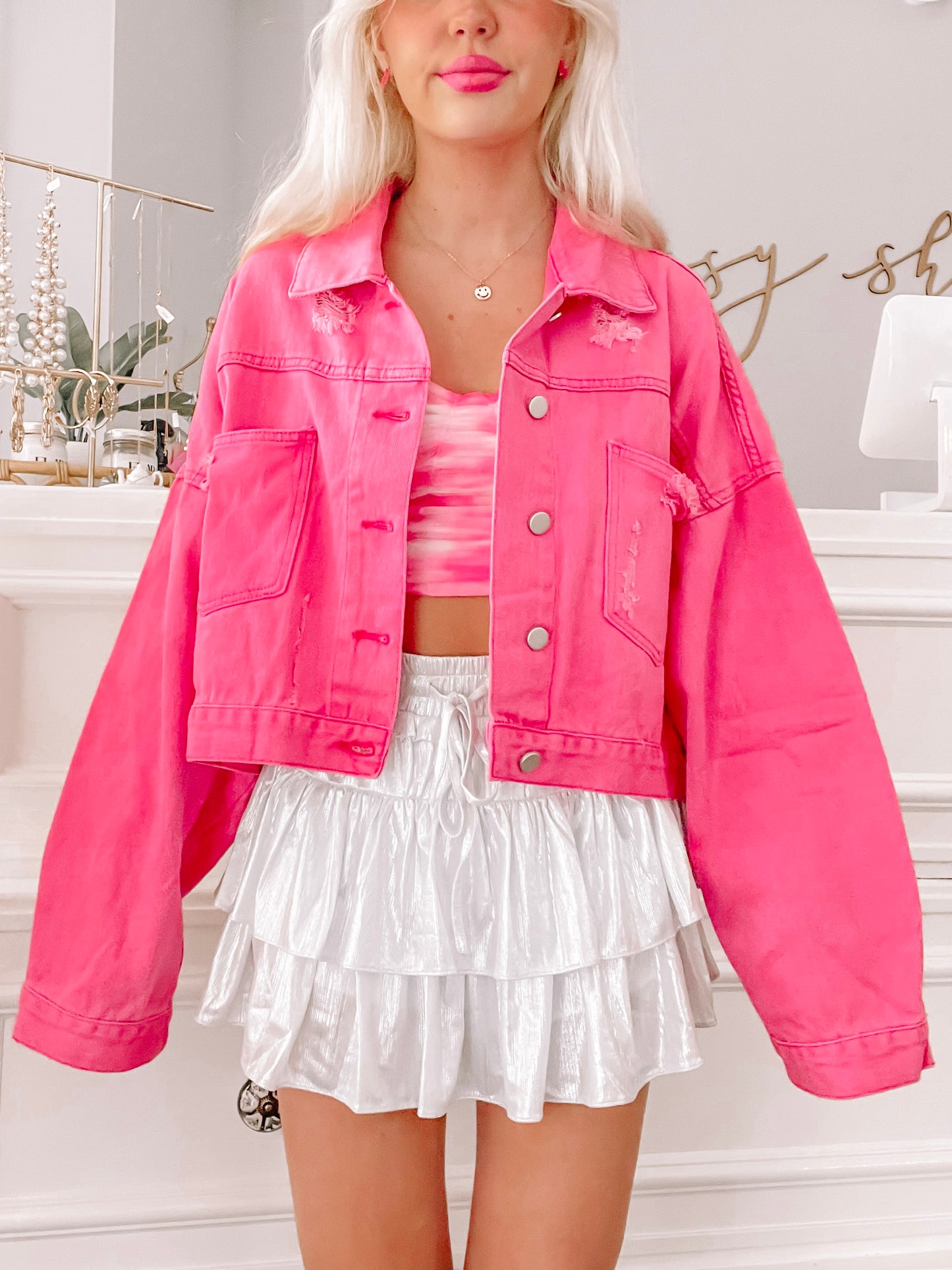 Hot pink denim jacket with distressed details, modeled with a white skirt.
