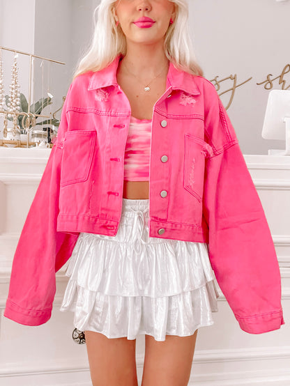 Hot pink denim jacket with distressed details, modeled with a white skirt.
