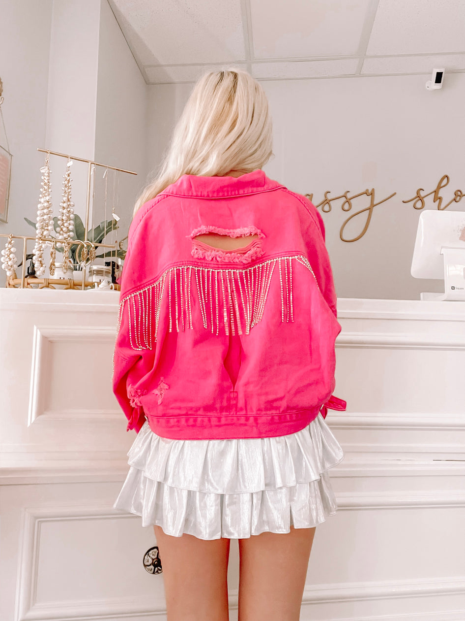 Hot pink denim jacket with rhinestone fringe, distressed detail, shown on model in store.
