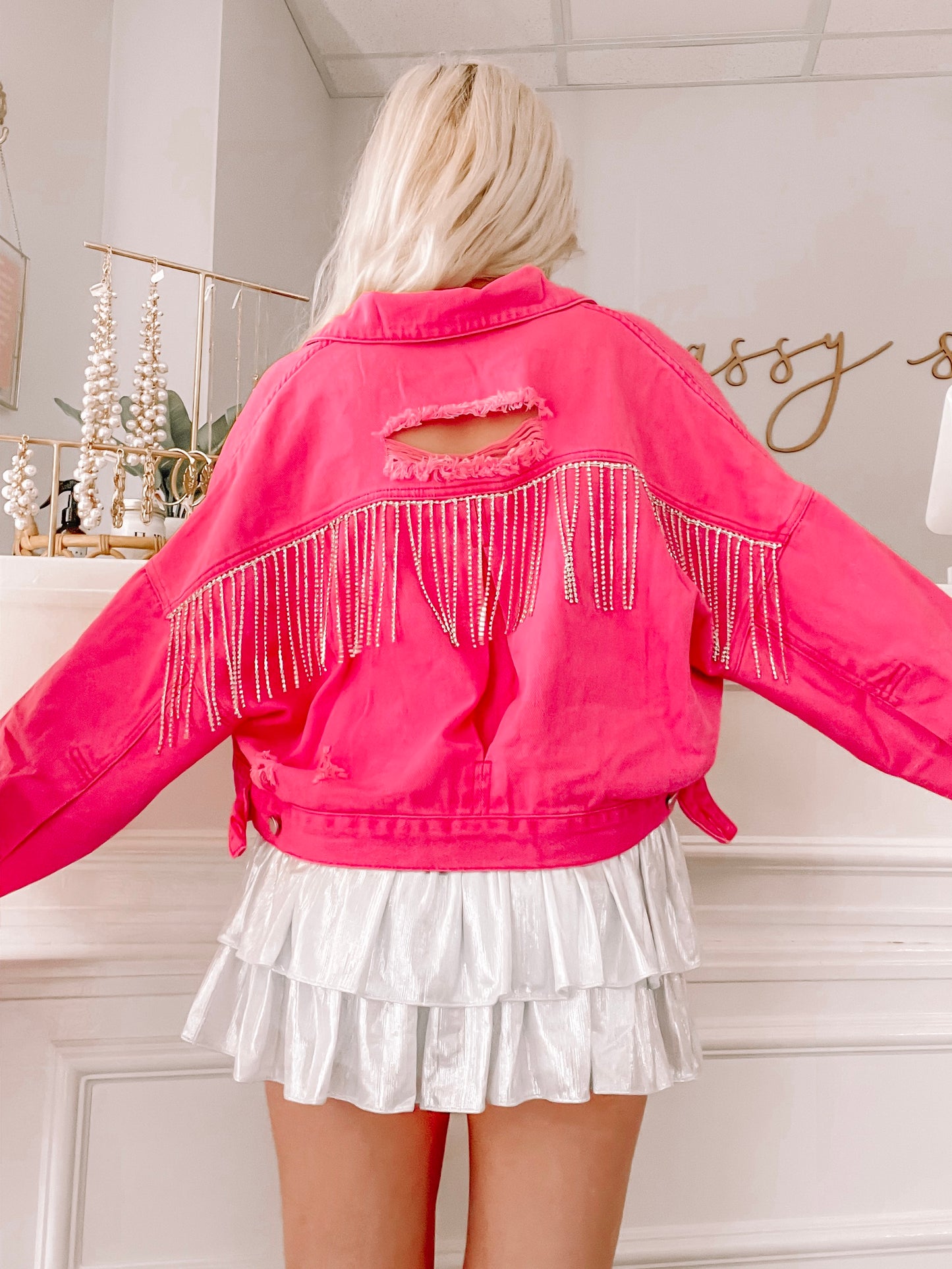 Hot pink denim jacket with distressed detailing and rhinestone fringe, shown from the back.
