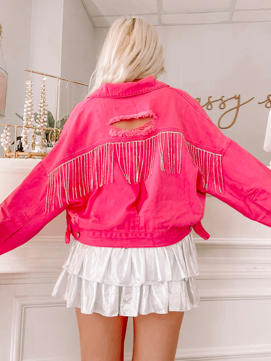 Hot pink denim jacket with distressed detailing and rhinestone fringe, shown from the back.
