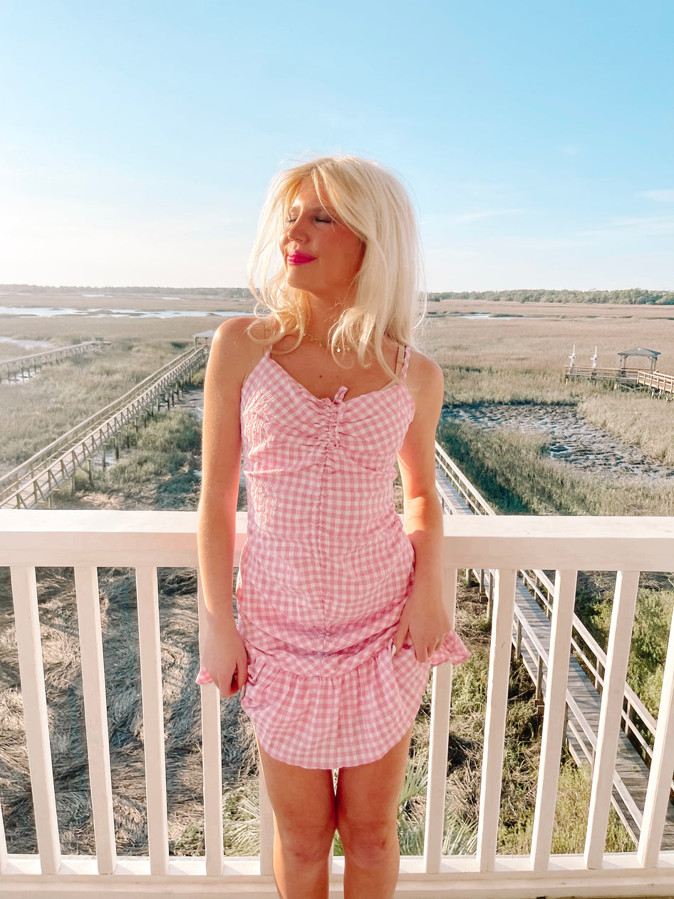 Pink gingham mini dress on a deck overlooking marshland.
