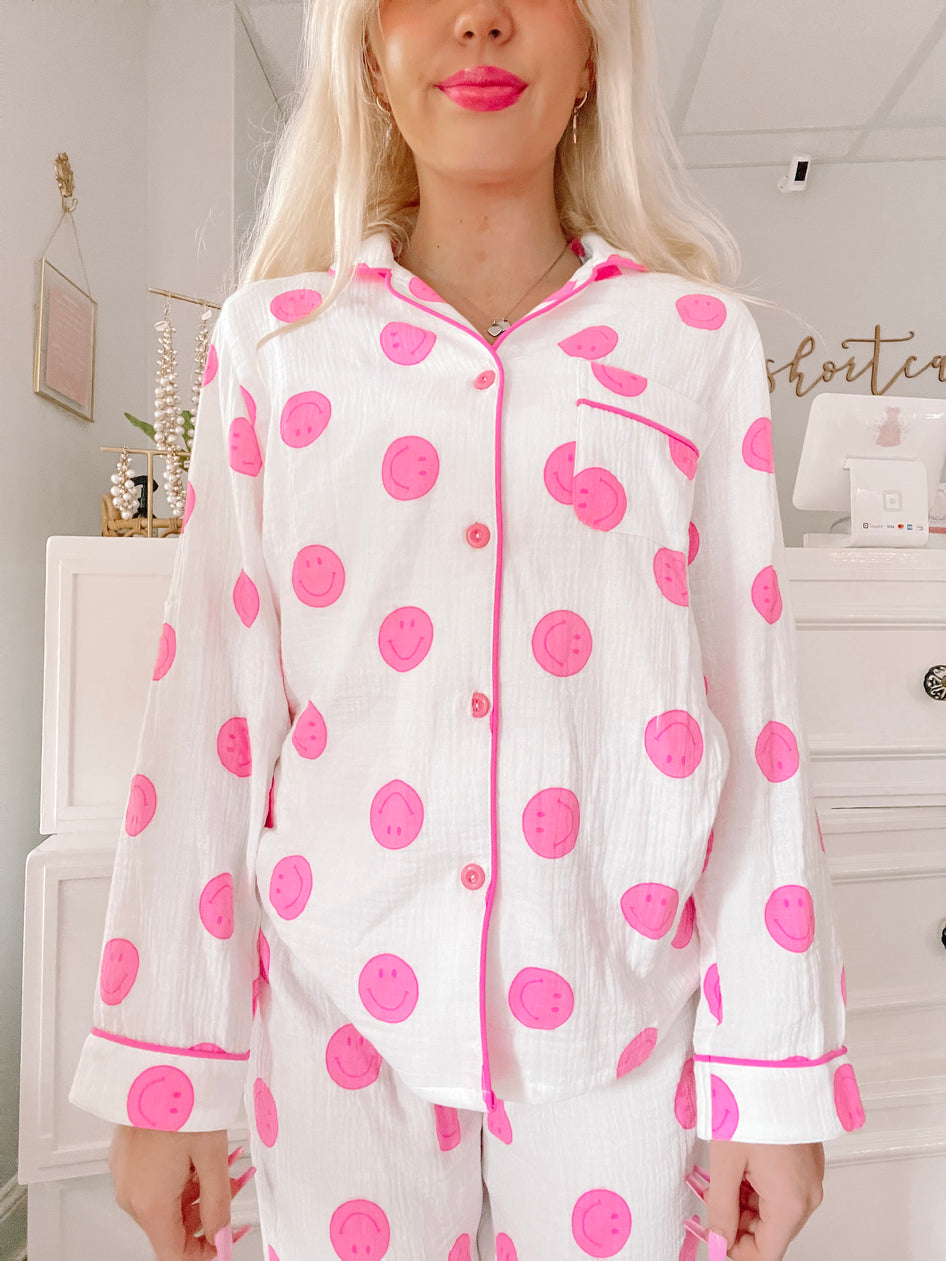 White pajama set with pink smiley faces, button-up top and long sleeves.
