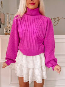 Bright pink ribbed knit turtleneck sweater with balloon sleeves, modeled with a white eyelet skirt.
