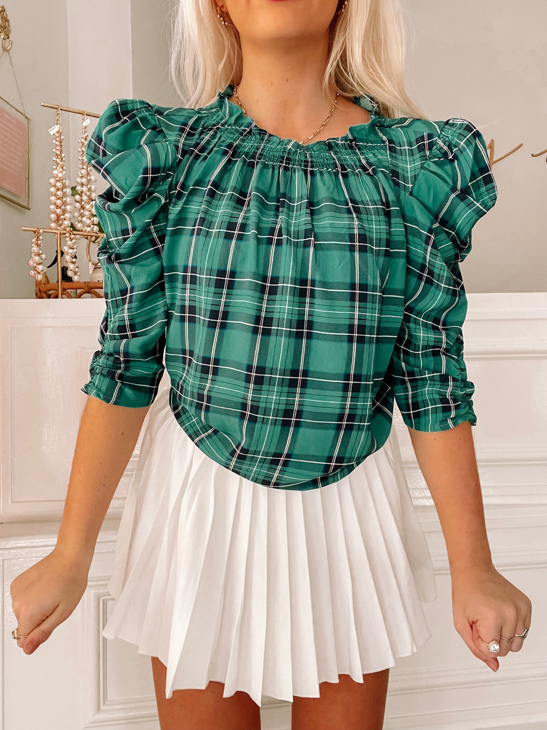 Green plaid blouse with puff sleeves, styled with a white pleated skirt.
