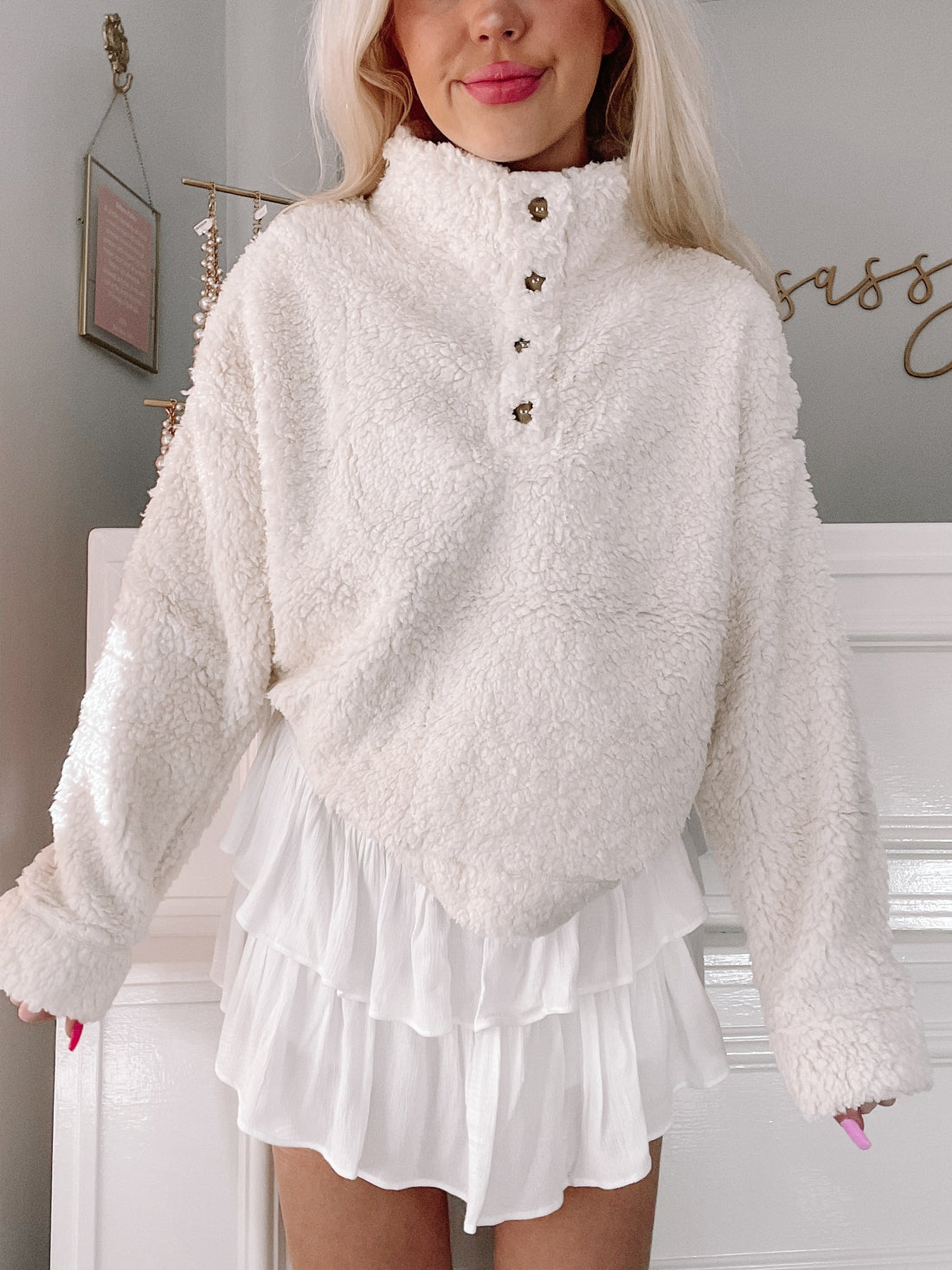 Cream-colored sherpa pullover with button placket, modeled with white ruffled shorts.
