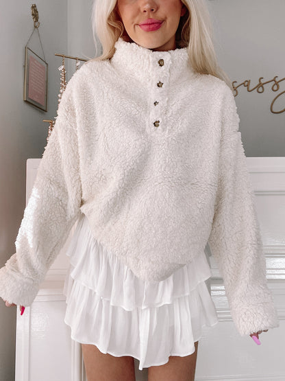 Cream-colored sherpa pullover with button placket, modeled with white ruffled shorts.
