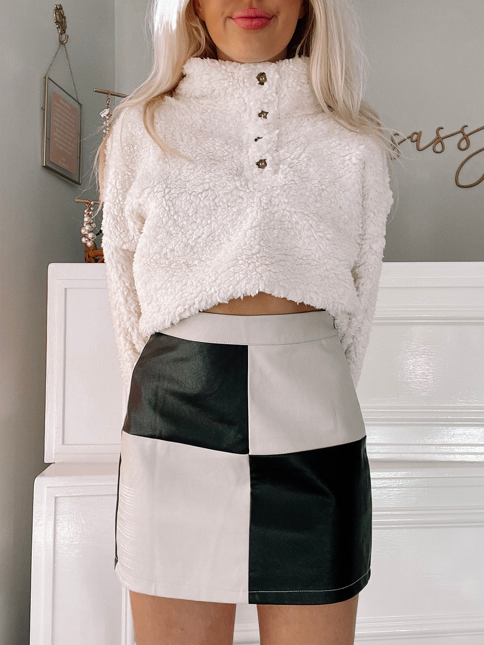 Chic black and cream faux leather mini skirt, checkerboard pattern, modeled against a white backdrop.
