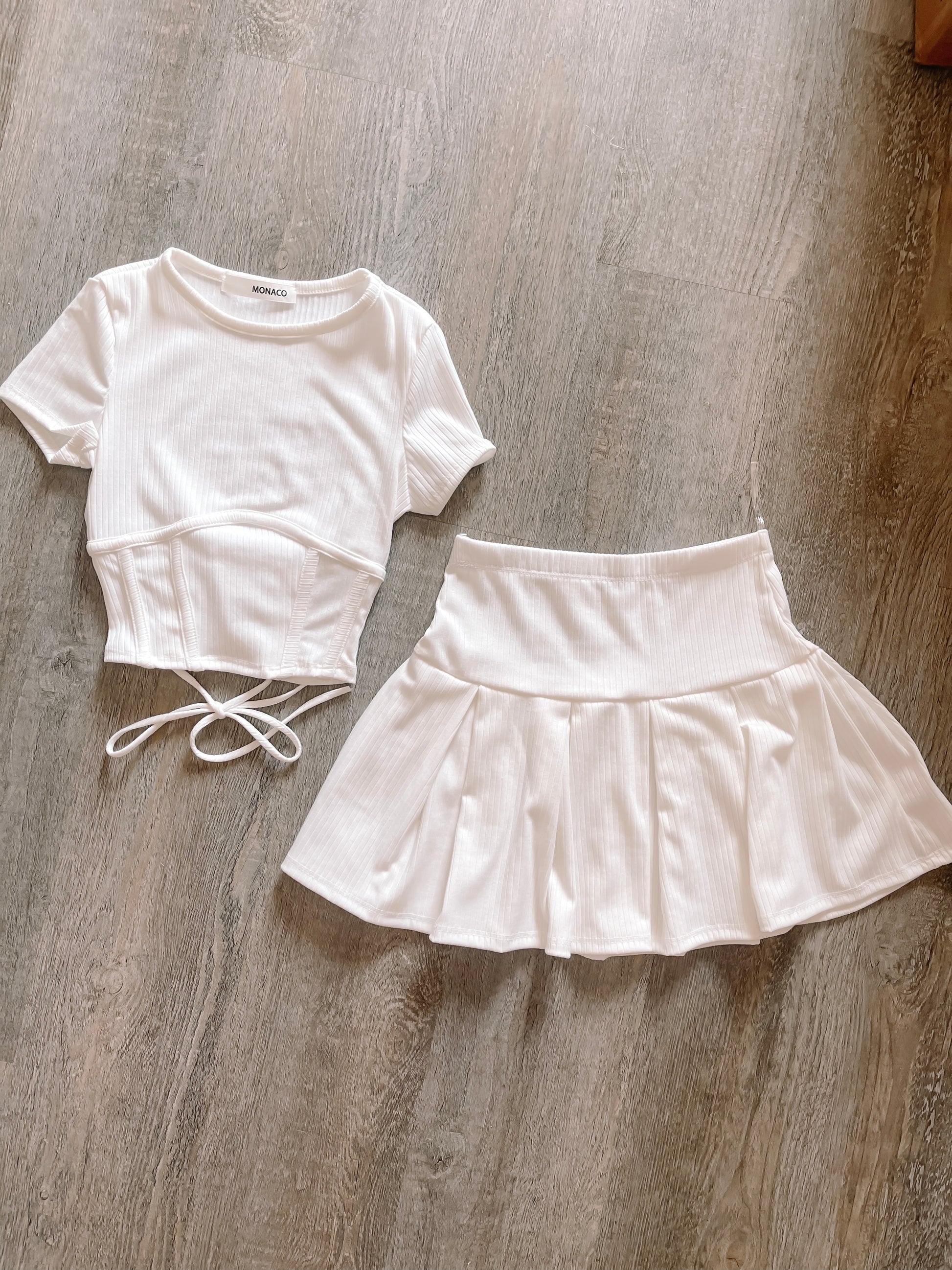 White ribbed knit crop top and pleated mini skirt set, laid flat on wood.
