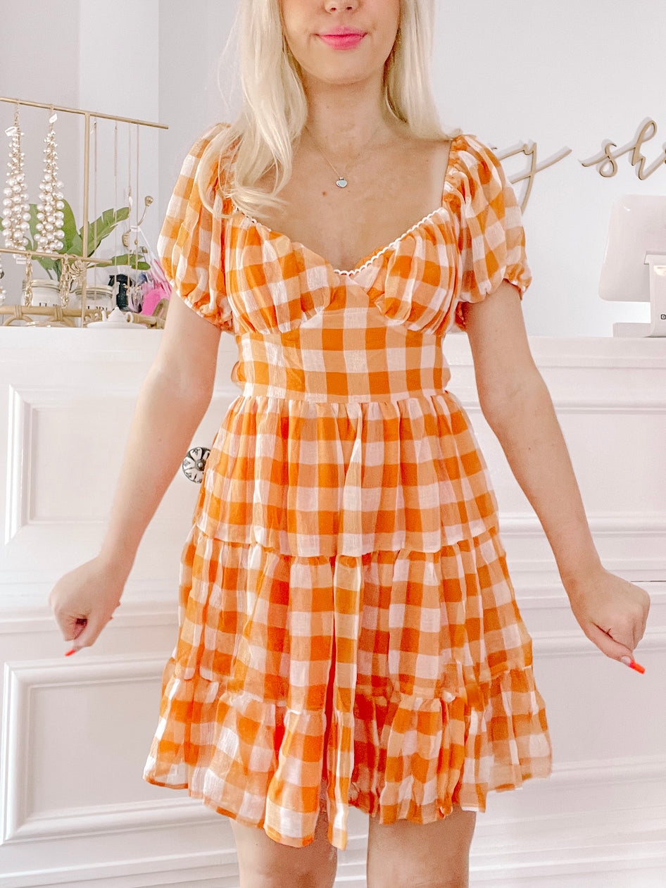 Orange and white gingham mini dress with puff sleeves and tiered skirt.
