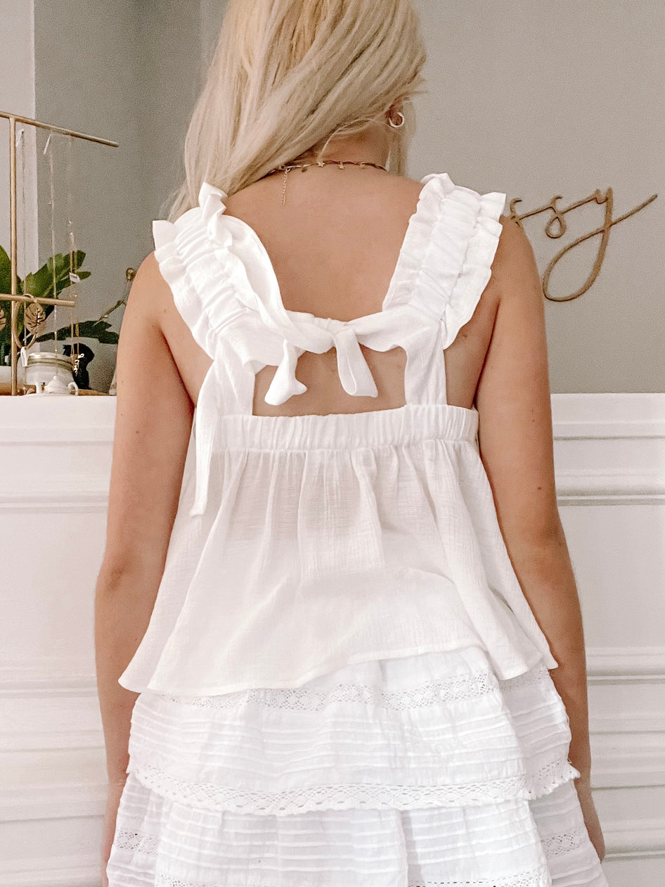 White eyelet peasant top with ruffled straps, tied at the back, shown on model.
