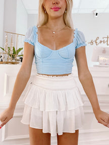 Light blue crop top with puff sleeves and white tiered ruffle mini skirt; summer fashion.
