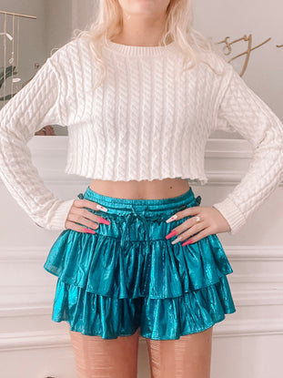Teal shimmer skirt with layered ruffles, styled with a white sweater.
