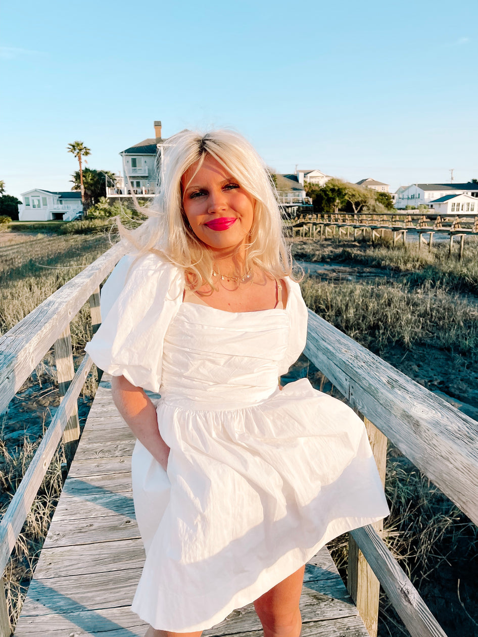 Woman in white puff-sleeve mini dress on boardwalk
