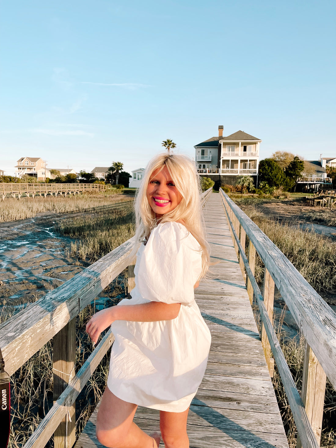 Woman in white puff-sleeve mini dress on a coastal boardwalk.
