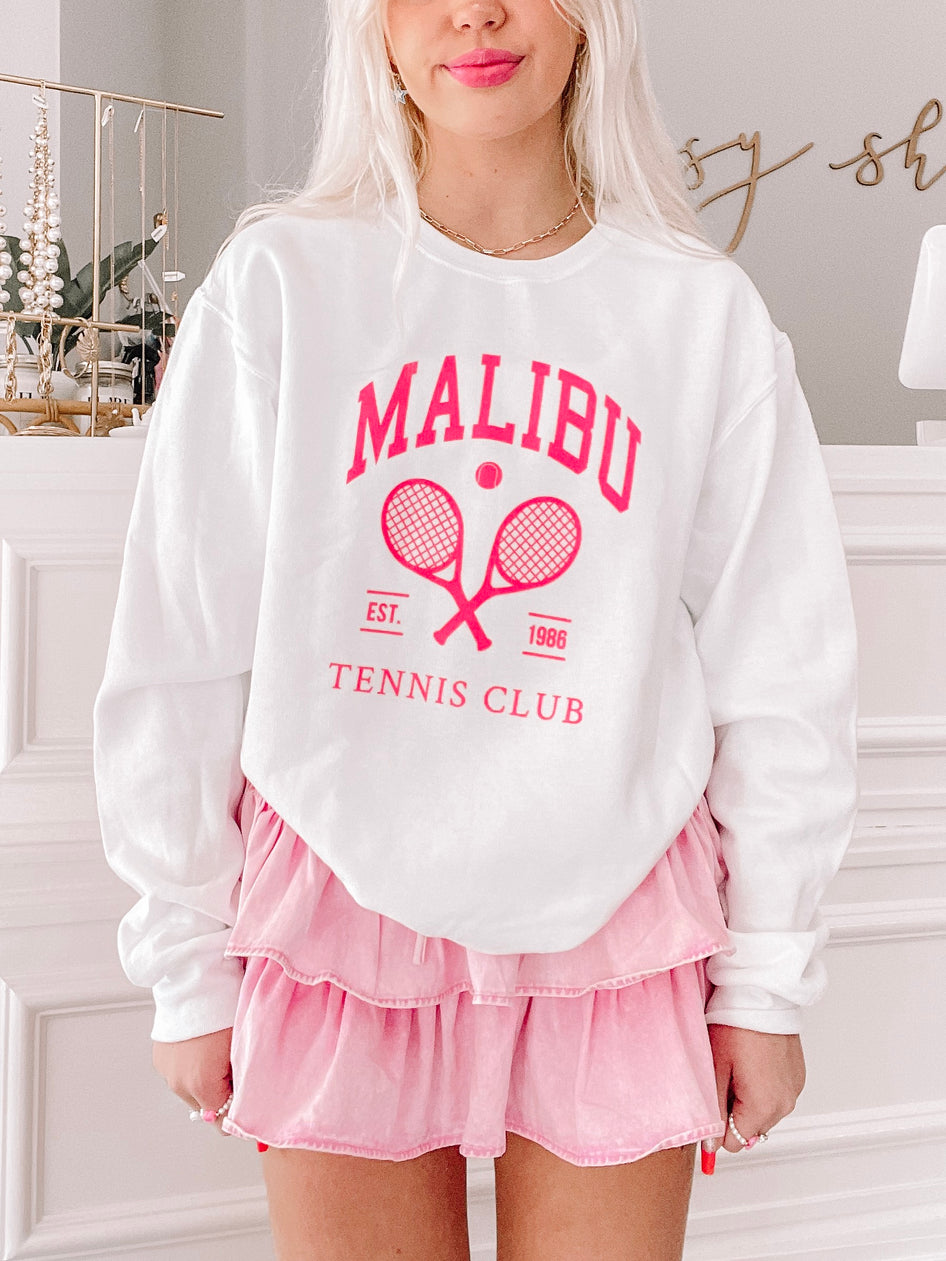 White crewneck sweatshirt with pink tennis club graphic; model wears pink skirt.

