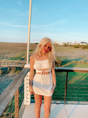 White cutout mini dress on a deck overlooking a coastal marsh.
