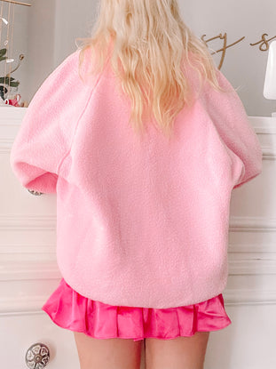 Bubblegum pink fleece jacket, shown from the back, paired with a hot pink pleated mini skirt.
