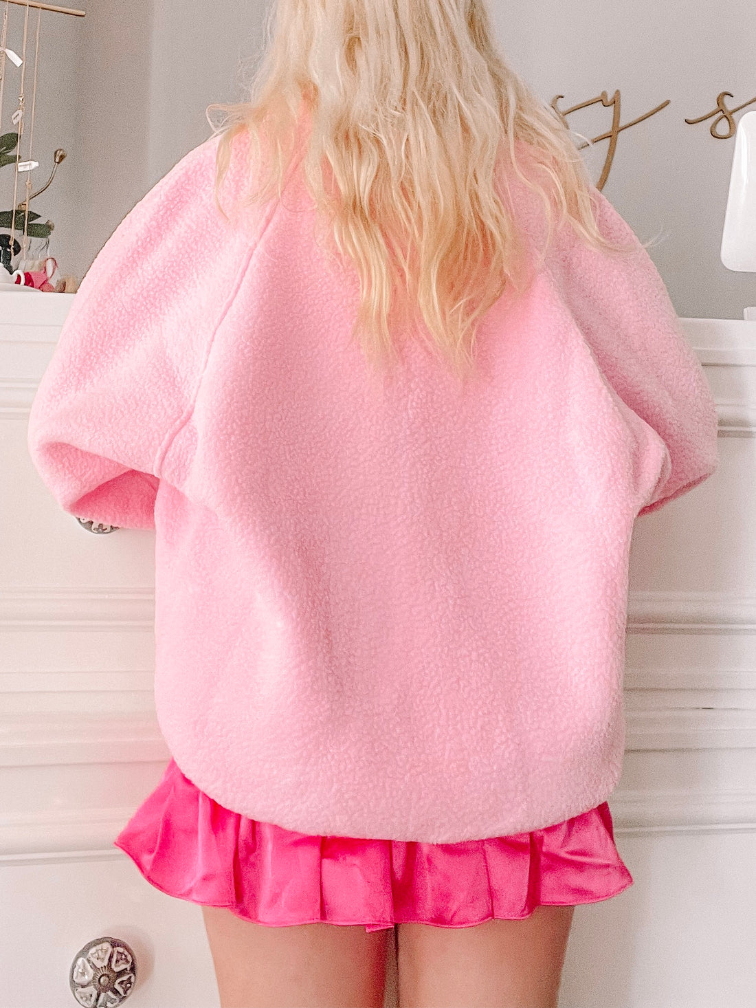 Bubblegum pink fleece jacket, shown from the back, paired with a hot pink pleated mini skirt.
