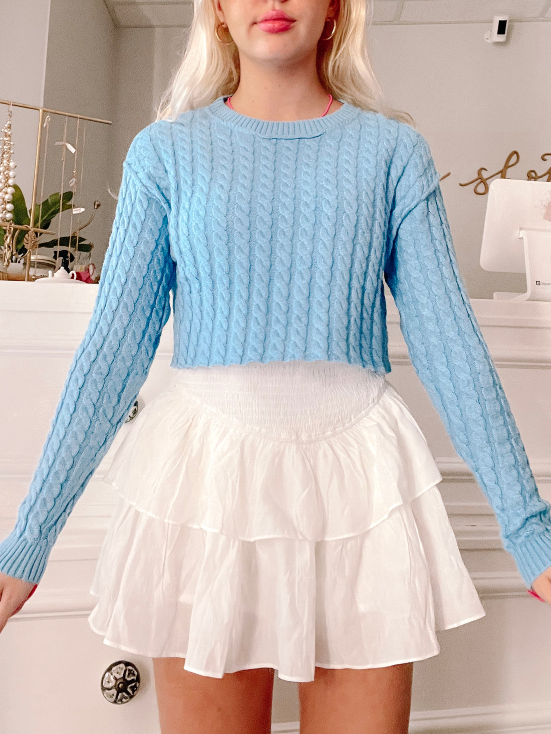 Light blue cable-knit cropped sweater paired with a white tiered mini skirt.
