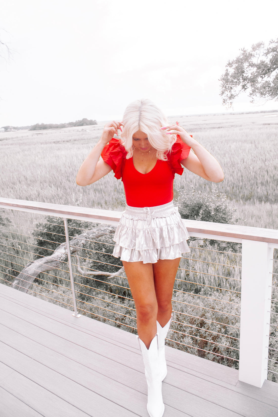 Red ruffled bodysuit styled outdoors, paired with a metallic skirt and white boots.
