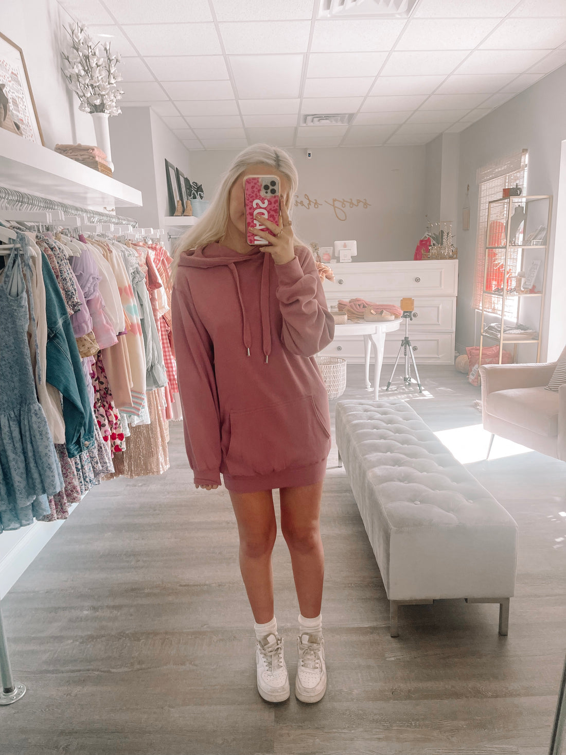 Dusty rose hoodie dress modeled in a boutique;  soft fabric, oversized fit.
