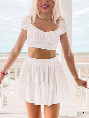 White crop top and tiered mini skirt set, worn outdoors near water.
