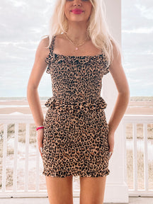 Brown and black leopard print mini skirt with smocked waist, ruffles, and a summery outdoor setting.
